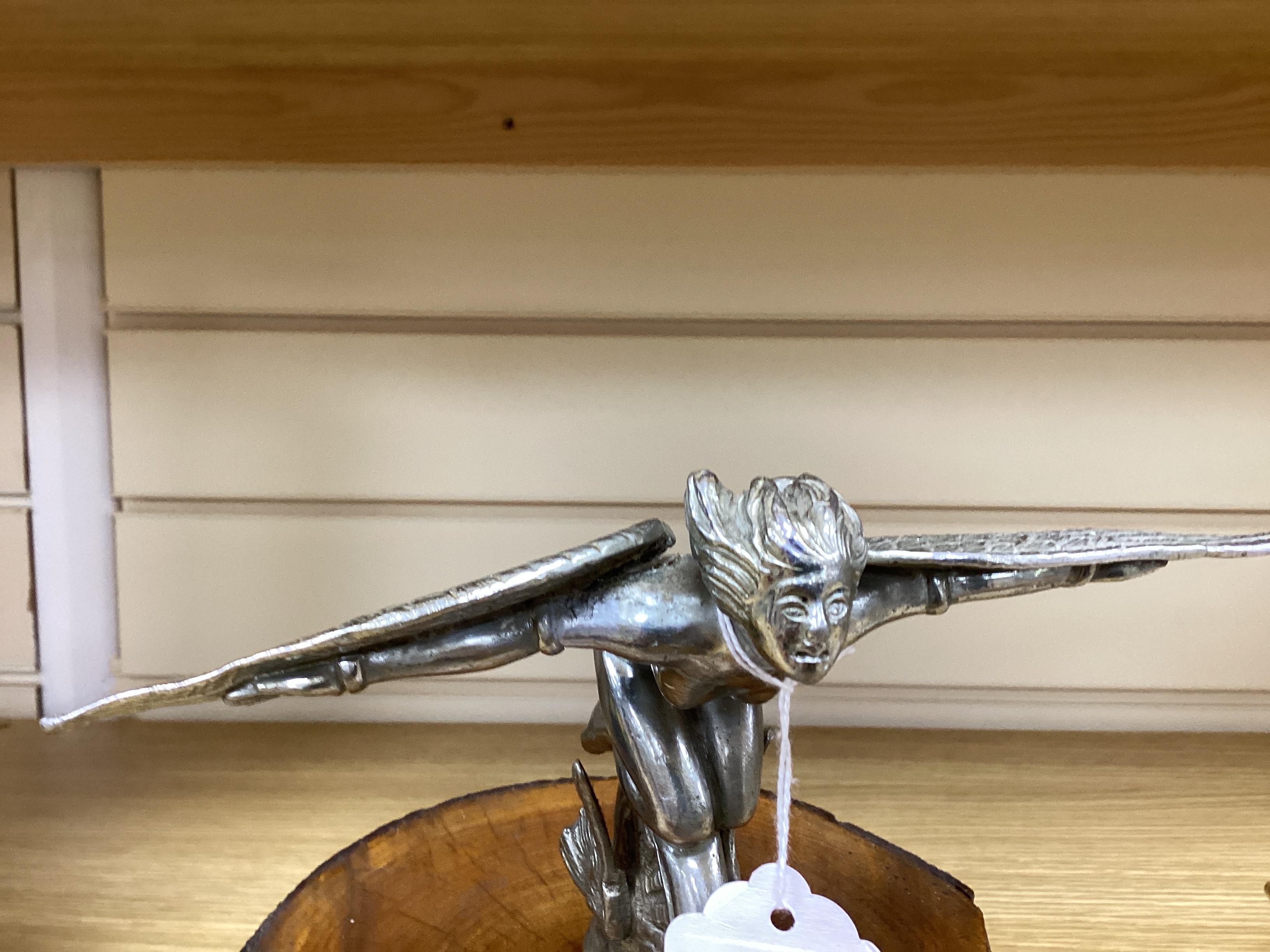 A vintage chrome plated car mascot of a winged female riding a wheel, mounted on a tree trunk cross-section, 19cm high